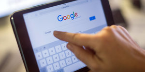 Eine Hand tippt auf ein Tablet etwas in die Suchmaschine Google ein