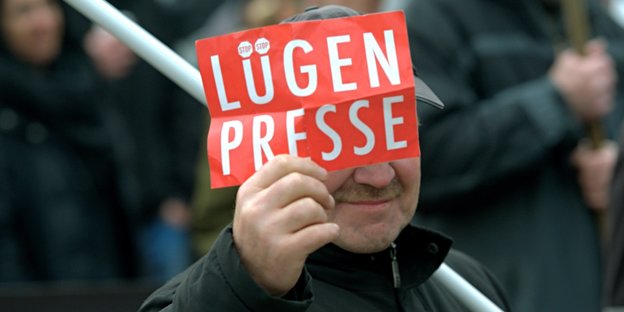 Ein Mann hält eine Karte mit der Aufschrift "Lügenpresse" hoch