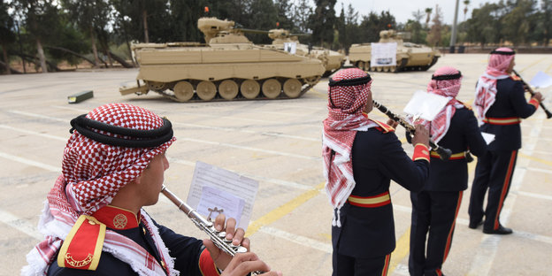Vier Beduinen mit Querflöten und Klarinetten vor einem Schützenpanzer