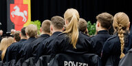 Junge Polizeianwärter sitzen bei einem Festakt zur Vereidigung in der Swiss Life Hall.