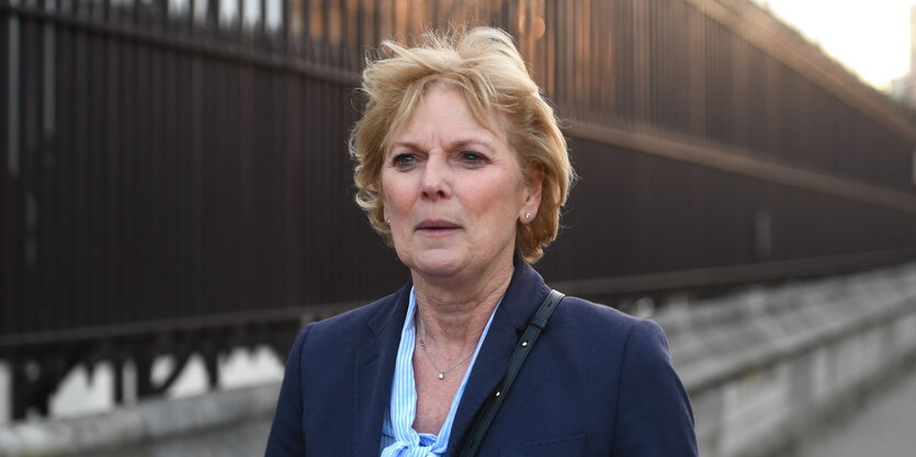 Anna Soubry, eine Frau mit blauem Jackett und blonden kurzen Haaren, läuft an einem hohen rostigen Zaun entlang