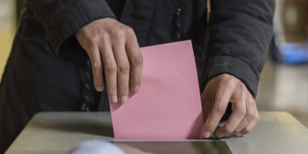 Ein Mensch wirft einen Wahlzettel in eine Wahlurne