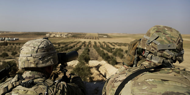 07.02.2018, Syrien, Manbij: Zwei US-Soldaten schauen von ihrer Basis in Syrien zur türkischen Grenze hinüber.