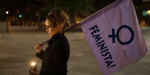 Eine Frau hat eine Kerze und eine lilafarbene Flagge mit dem Schriftzug "Feminista" in der Hand