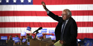 Bernie Sanders winkt vor einer großen US-amerikanischen Flagge