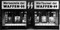 Schwarz-Weiß-Aufnahme: In einer Ladenfläche sind die Schriftzüge "Werbestelle der Waffen-SS" auf Deutsch und Belgisch zu sehen, im Schaufenster sind Bilder von SS-Angehörigen zu sehen