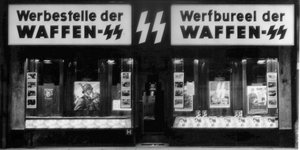 Schwarz-Weiß-Aufnahme: In einer Ladenfläche sind die Schriftzüge "Werbestelle der Waffen-SS" auf Deutsch und Belgisch zu sehen, im Schaufenster sind Bilder von SS-Angehörigen zu sehen