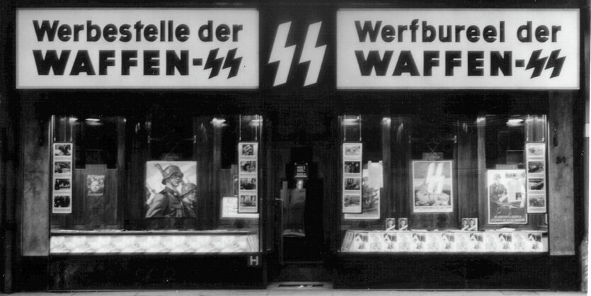 Schwarz-Weiß-Aufnahme: In einer Ladenfläche sind die Schriftzüge "Werbestelle der Waffen-SS" auf Deutsch und Belgisch zu sehen, im Schaufenster sind Bilder von SS-Angehörigen zu sehen