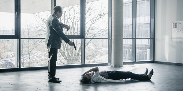 Ein Mann richtet eine Pistole auf eine am Boden liegende Frau