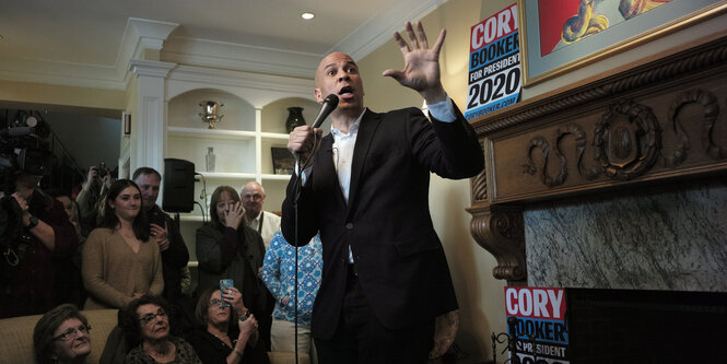 Ein Mann, Cory Booker, hält eine Rede in einer Art Kaminzimmer, mehre Menschen schauen ihn an