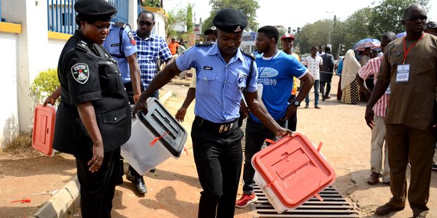 Polizisten tragen versiegelte Wahlurnen aus Plastik