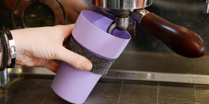 ein lilafarbener Plastikbecher unter einer Kaffeemaschine