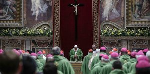 Viele Geistliche in grüner Robe hören in der Kirche dem Papst zu.
