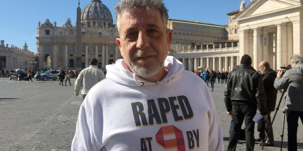 Piero Brogi, Missbrauchsopfer aus Italien, steht auf dem Petersplatz in Rom, er trägt ein T-Shirt mit der Aufschrift "Raped at 9" (Vergewaltigt mit neun Jahren)