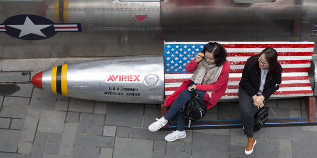 Zwei Frauen sitzen auf einer Bank, die mit der US Flagge dekoriert ist