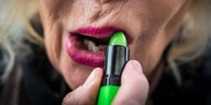 Eine Frau zieht mit ihrem grünen Lippenstift die roten Lippen nach