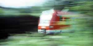 Ein verschwommenes Foto zeigt einen Regionalzug, der vor Pflanzen fährt