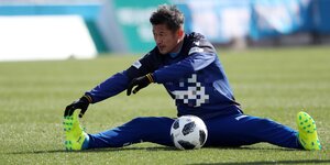 Der japanische Fußballer Miura sitzt auf dem Fußballfeld und vor ihm liegt ein Fußball