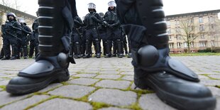 Nahaufnahme von Polizeistiefeln, dahinter einige PolizistInnen in Sicherheitsmontur