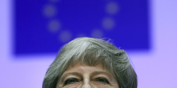 Nahaufnahme von der oberen Hälfte von Theresa Mays Gesicht vor einer EU-Flagge