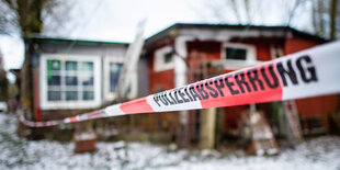 absperrband mit dem schriftzug "Polizeiabsperrung" vor der holzhütte des hauptverdächtigen im schnee