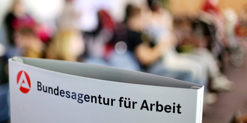 Ein Schild mit der Aufschrift «Bundesagentur für Arbeit» steht einem vollen Wartezimmer im Jobcenter.