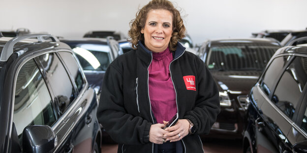 Frau steht zwischen vielen Autos in einem Raum Frau steht zwischen vielen Autos in einem Raum