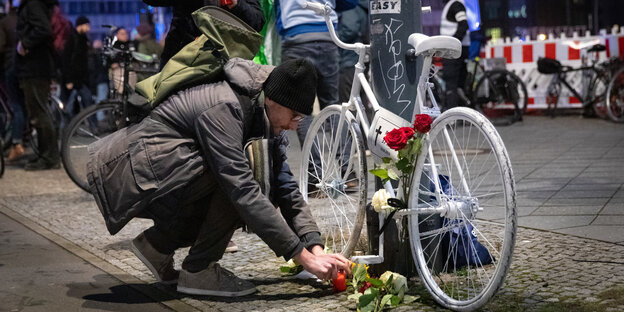 Ein Mann legt Blumen an ein weißes Fahrrad