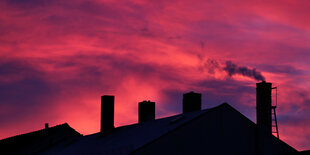 Aus einem Kamin steigt Rauch in einen roten Abendhimmel