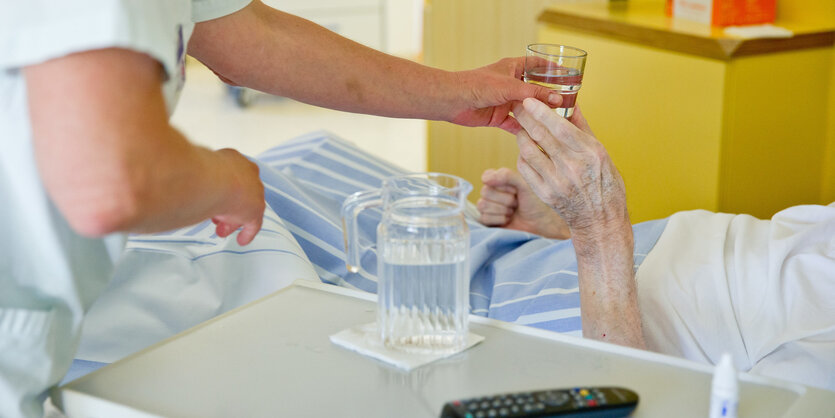 Eine Pflegerin gibt einer im Krankenbett liegenden Person Medizin