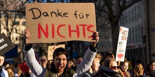 Ein Student hält während einer Demo ein Schild hoch, auf dem „Danke für Nichts“ steht