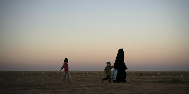 Eine Frau in Niqap läuft mit zwei Kindern durch die Landschaft.