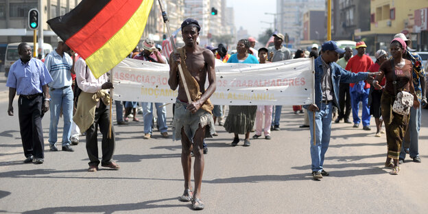 Eine Demo in Mosambik, voraus läuft ein Demonstrant, der eine Deutschlandfahne trägt