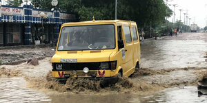 ein vollbesetzter Kleinbus fährt eine überschwemmte Straße entlang