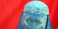 eine Frau unter einer blauen Burka vor totem Hintergrund