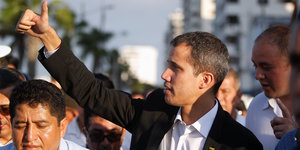 Ein Mann mit sehr kurzen Haaren, Juan Guaido, steht inmitten von Menschen und hält den Daumen nach oben