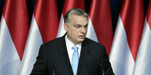 Viktor Orbán, ein Mann in Anzug und Krawatte, vor rot-weißen Flaggen