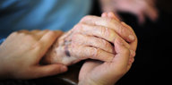 Zwei Hände halten die Hand einer älteren Person