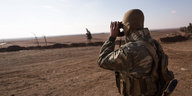 YPG-Soldat steht auf einer freien Fläche in Syrien und blickt durch ein Fernglas