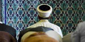 Betende Menschen stehen mit dem Rücken zum Bild hinter einem Imam