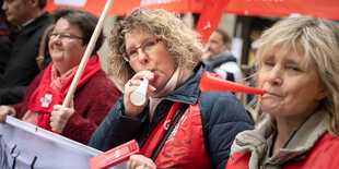 drei erzieherinnen und lehrerinnen mit trillerpfeifen und plakaten bei einem warnstreik während des tarifstreits