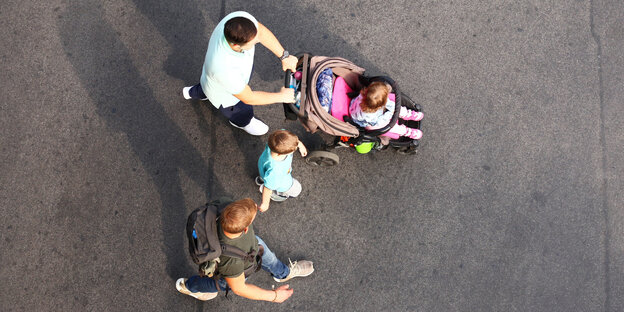 Zwei junge Männer gehen mit zwei Kindern über eine Straße. Eines der Kinder, ein kleines Mädchen, sitzt dabei in einem Kinderwagen.
