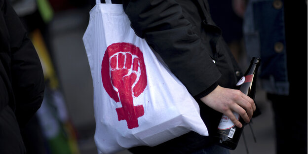 ein stoffbeutel mit einem feministischen symbol, eine geballte faust in dem symbol für frau, hängt einer person über die schulter