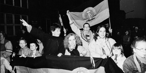 Schwarz-Weiß-Aufnahme: Junge Frauen und Männer halten DDR-Fahnen in die Luft