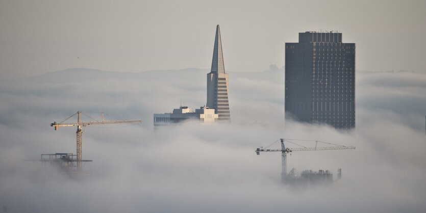 Hochhäuser und zwei Kräne ragen aus den Wolken über einer Stadt hervor