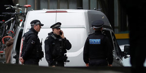 Drei britische Polizisten stehen vor einem silbernen Van, einer von ihnen telefoniert