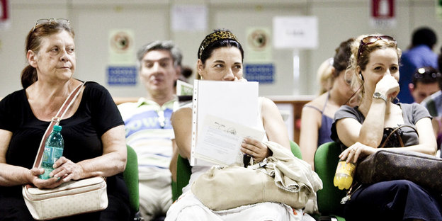Drei Frauen sitzen in einem Wartezimmer und halten Dokumente in den Händen