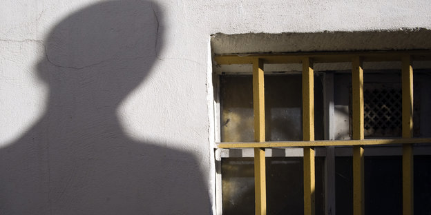 Der Schatten eines Mannes neben Gitterfenstern