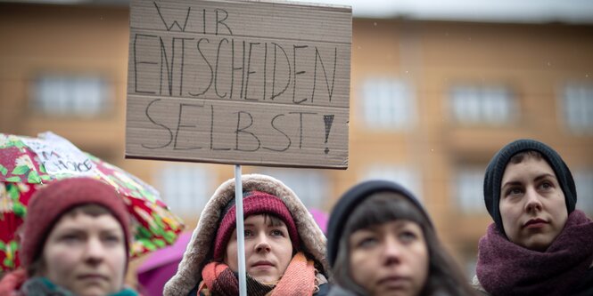 Vier Frauen halten ein Schild mit der Aufschrift "Wir entscheiden selbst!" hoch