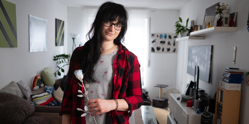 Eine Frau steht mit einer weißen Rose in ihrer Hand in einem Wohnzimmer